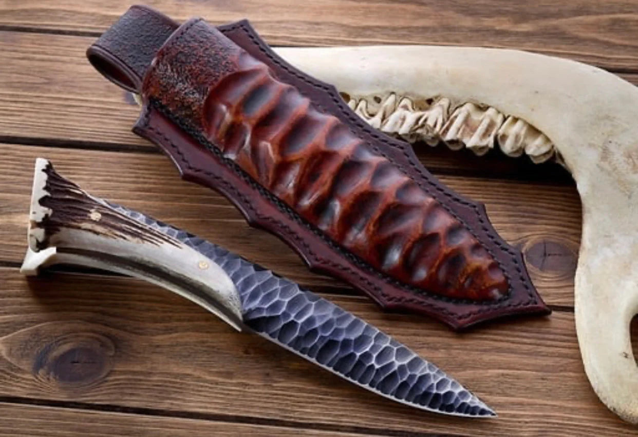 Custom forged 1095 high carbon steel hunting knife with antler horn handle, featuring a leather sheath