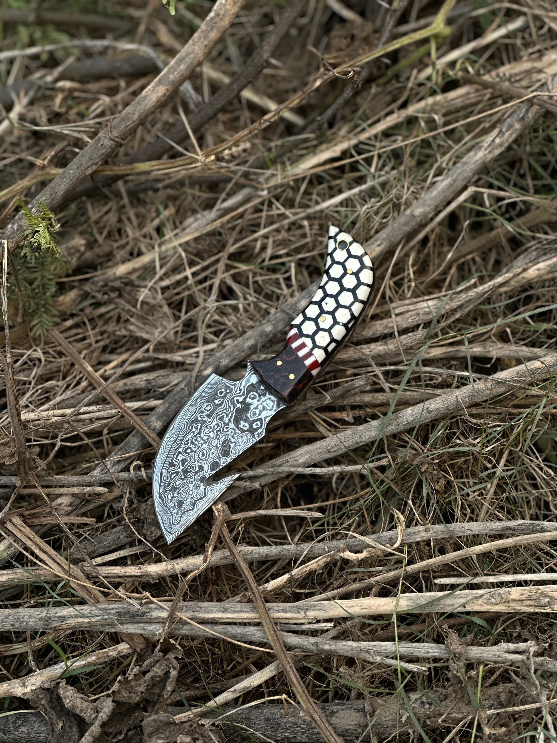 7.5” Damascus steel guthook knife featuring a rosewood and resin handle with a leather sheath.