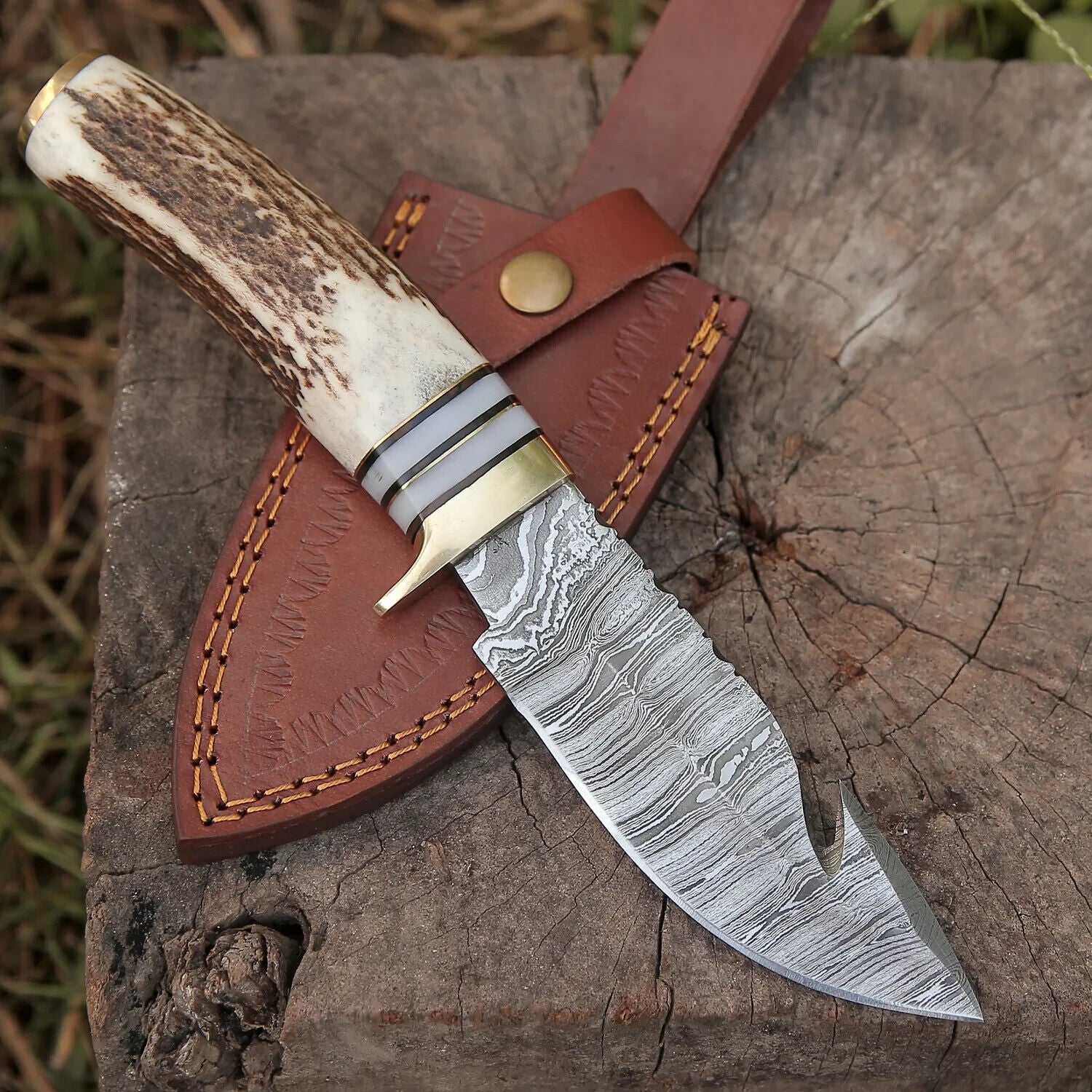 "Damascus steel guthook knife with stag horn handle and brass guard, displayed with a leather sheath."