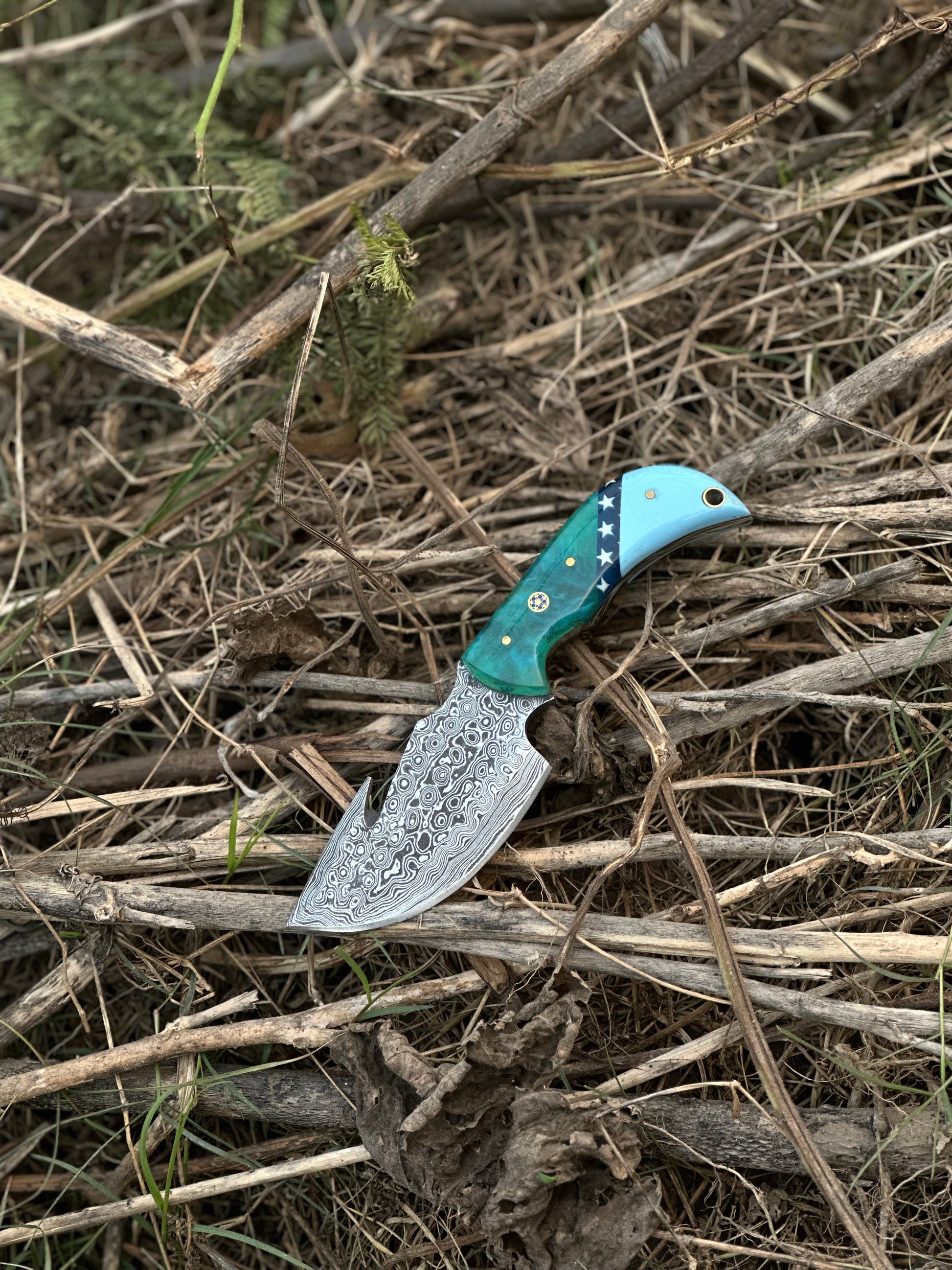 Handcrafted Damascus steel guthook skinning knife with a resin handle, perfect for precision tasks, with a leather sheath.