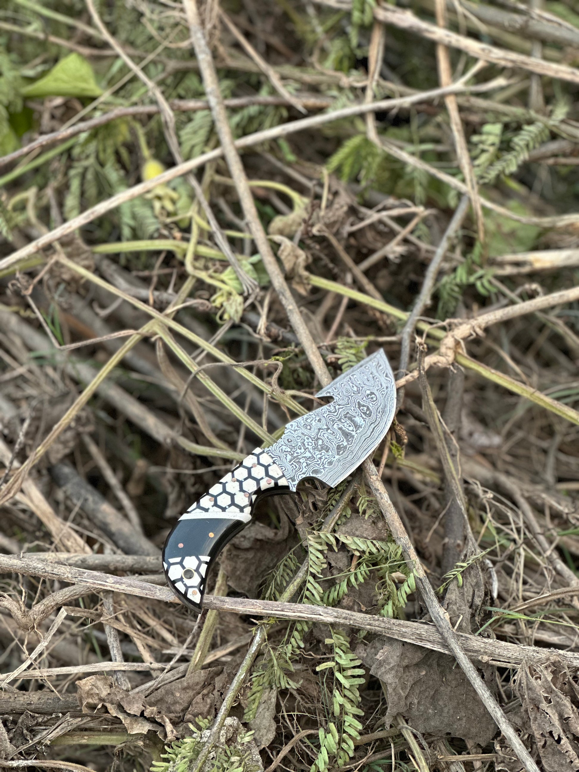 Unique Damascus steel guthook skinning knife featuring a custom resin handle, paired with a leather sheath.